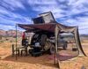 SUV in middle of desert with car awning, roof tent, and trail kitchen set up.