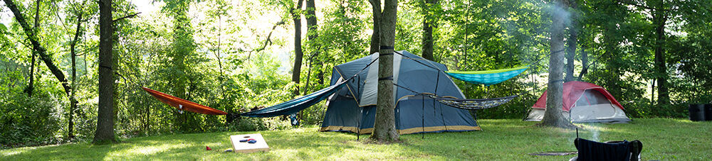 Tent camping in a wooded area with hammocks set up between trees.