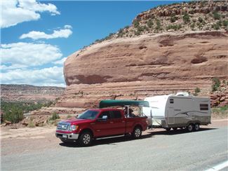 Red truck pulling white travel trailer with buttes in the background.