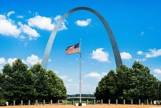 An American flag in front of the St. Louis Arch