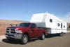 Red truck pulling a white fifth wheel camper with buttes in the background.