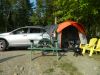 Car camping site with Silver SUV, set up tent, green picnic table, and yellow lawn chairs.