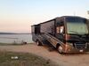 RV motorhome parked next to water during sunset.