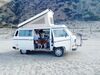 Old white van with pop up sitting on the beach.